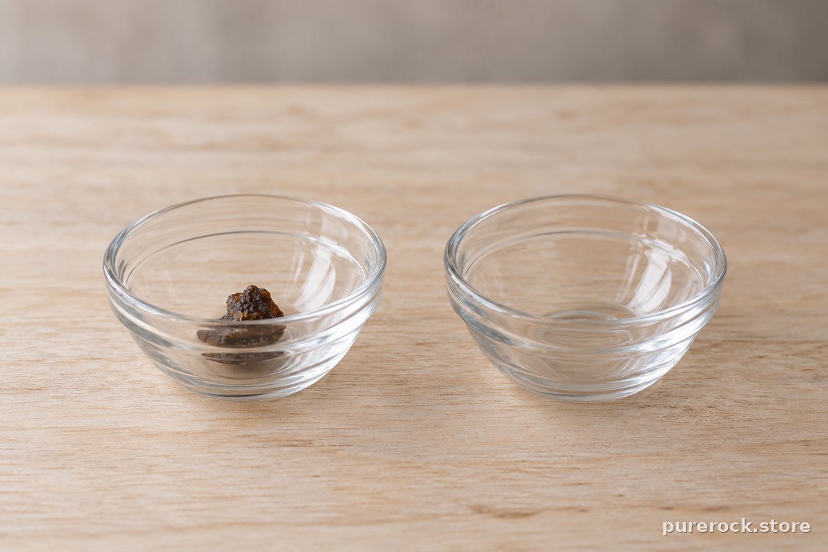 Two small identical glass bowls on a table, one holding a dark resin crumb and one empty, suggesting a blinded comparison