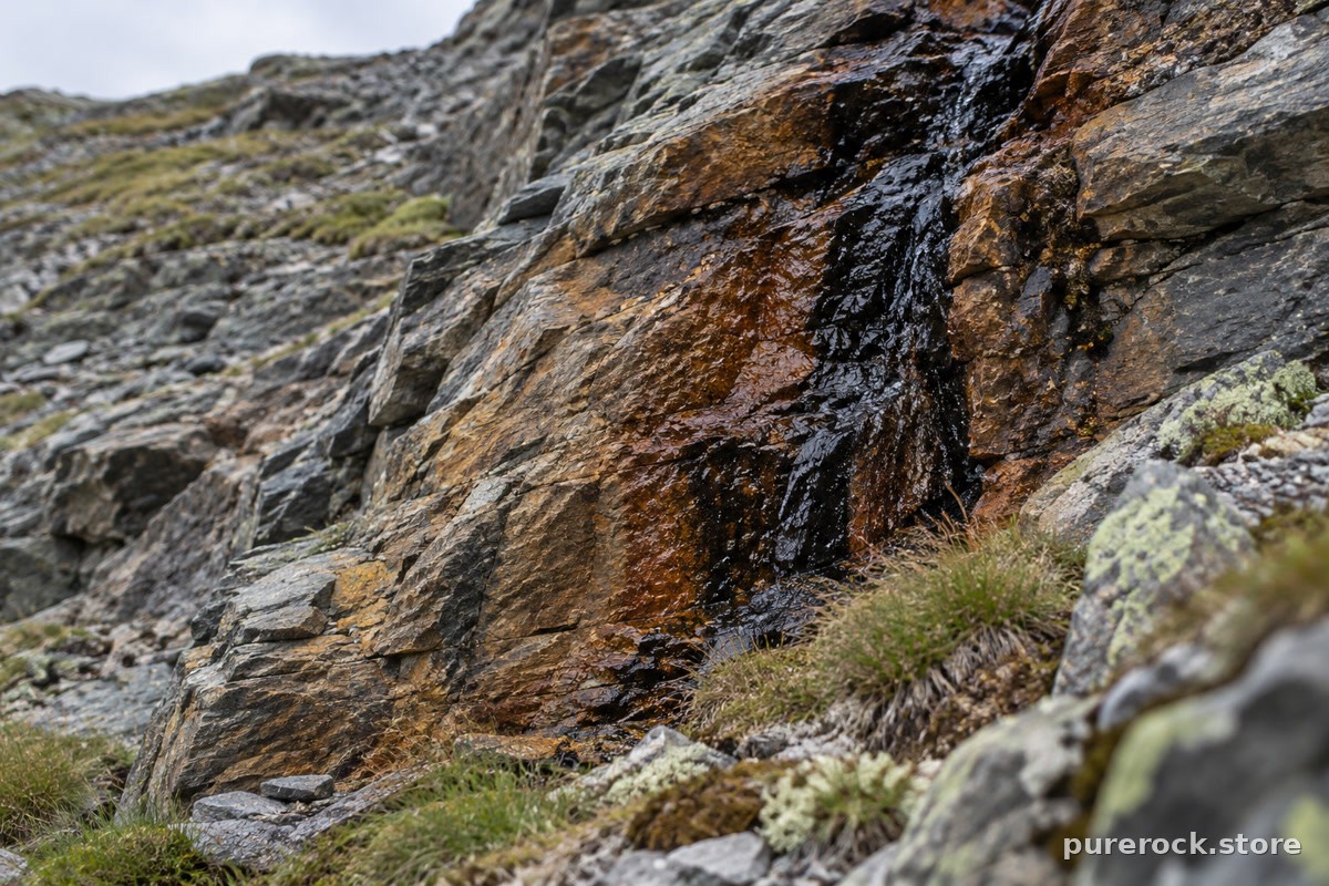 Layered mountain rock strata with a thin dark mineral seep running down a crack, illustrating where raw shilajit resin originates