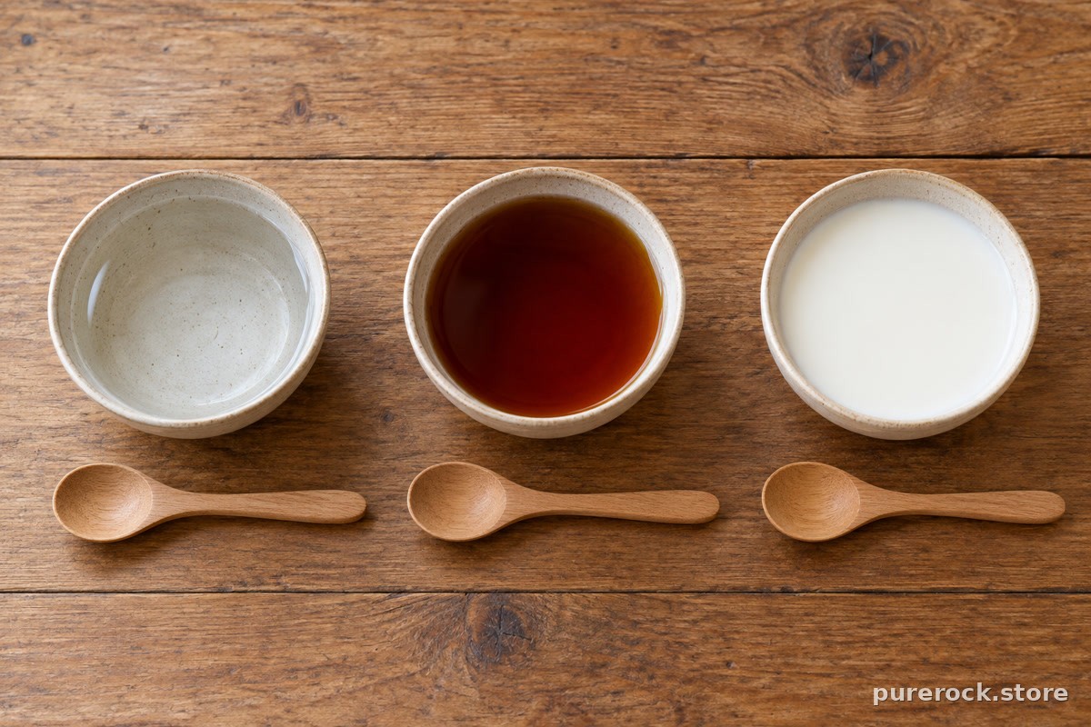 Three small bowls on a table holding warm water, black tea and milk, each beside a dry spoon, with no labels or text